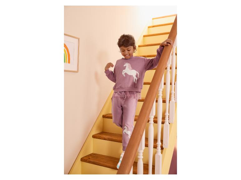 Fille en survêtement violet avec une licorne descendant les escaliers.