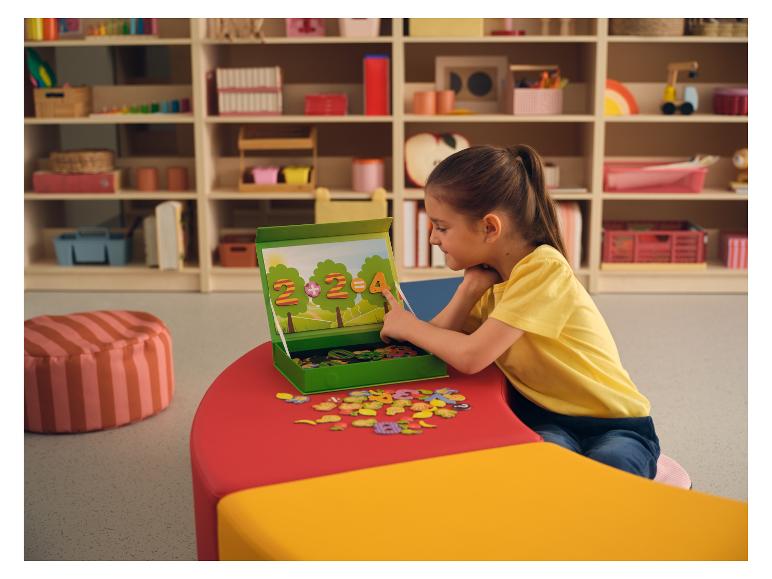 Fille jouant avec un puzzle magnétique de chiffres et de lettres sur une table colorée.