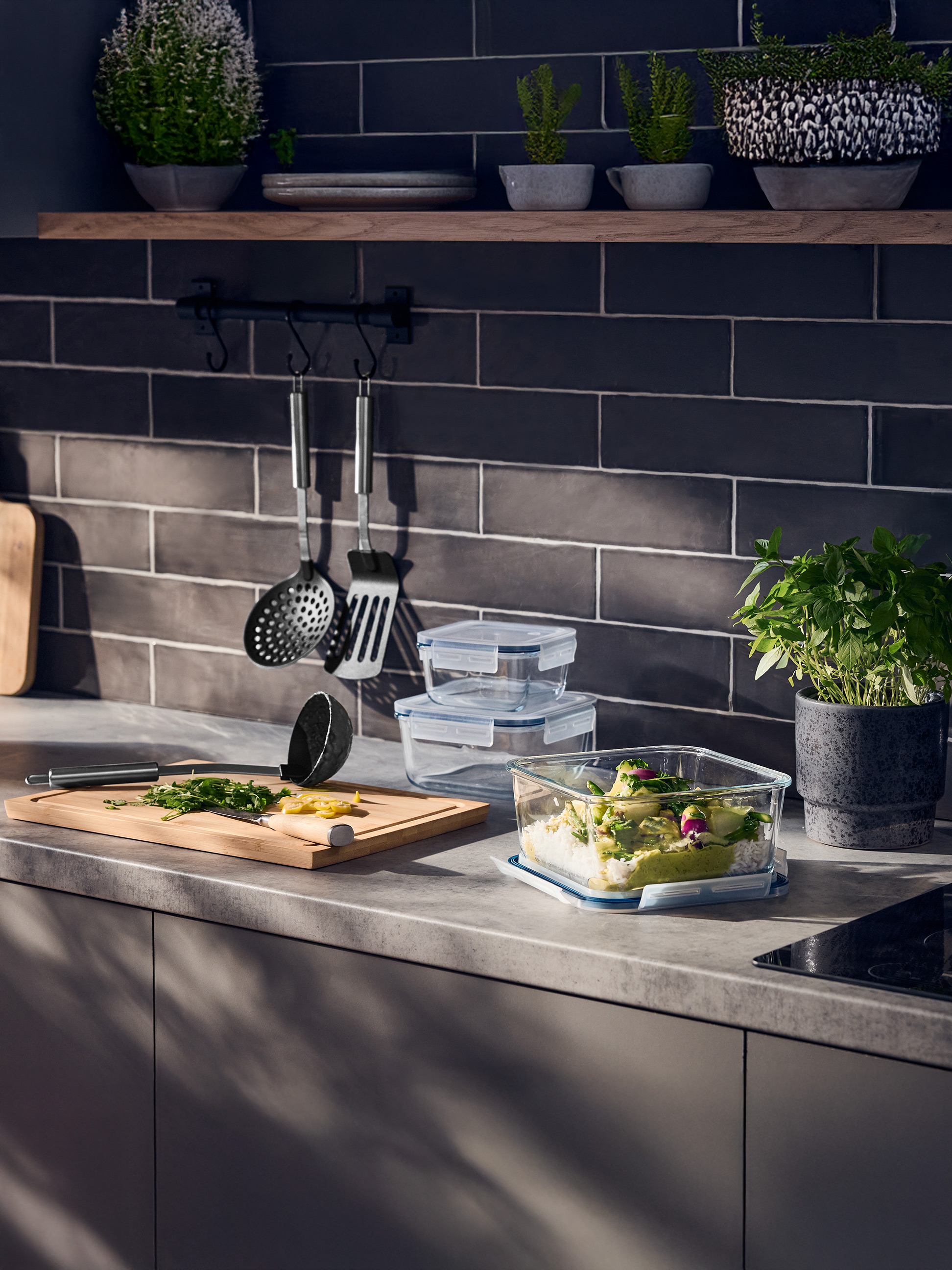 Comptoir de cuisine avec des récipients en verre pour aliments, une planche à découper et des herbes.