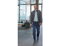 Homme en cardigan gris, polo bleu clair et jean, marchant dans un bureau.