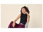 Femme souriante en débardeur noir et pantalon bordeaux assise sur une chaise.