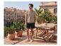 Homme en polo beige et short foncé sur une terrasse ensoleillée avec vue sur la ville.