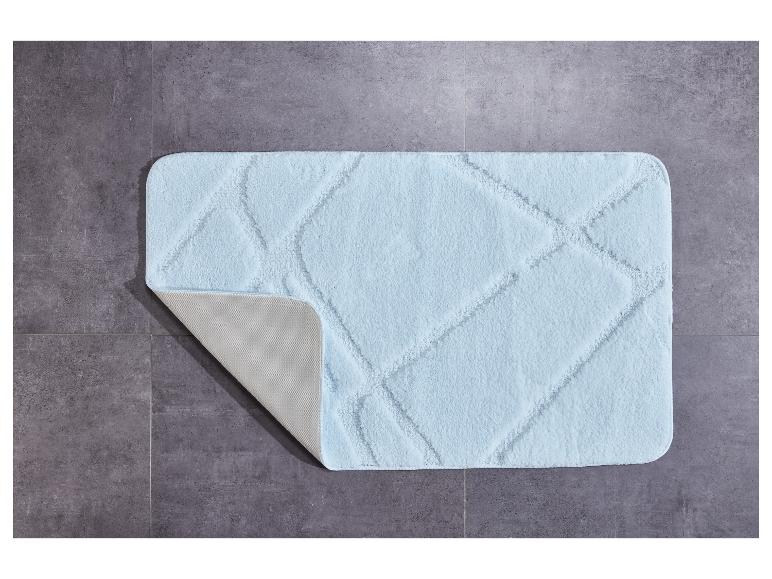 Un tapis de bain bleu clair avec un motif losange sur un sol en carrelage gris.