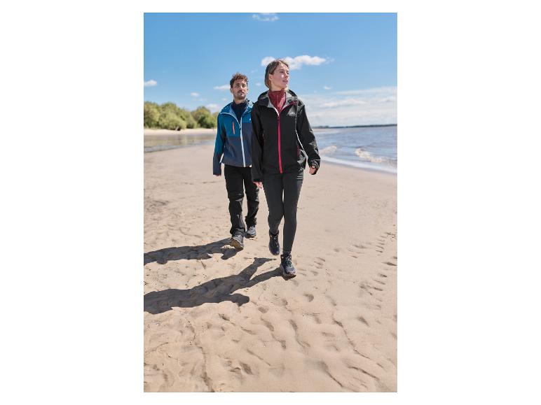 Une femme vêtue d'une veste technique premium CRIVIT se promène sur une plage de sable avec un homme.