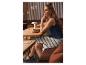Femme en robe rayée et sandales, sirotant un café dans un café.