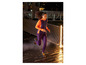 Une femme courant en vêtements de sport et chaussures de course, sur une surface mouillée la nuit.