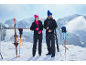 Couple en vestes polaires noires et pantalons de ski devant des montagnes enneigées.