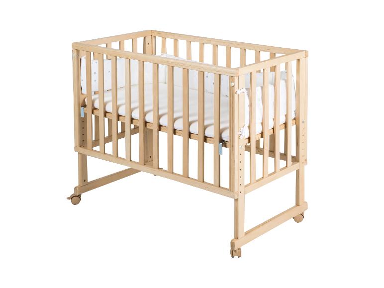 Lit bébé en bois avec literie blanche et hauteur réglable sur roulettes blanches.