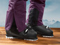 Des chaussures de ski avec un pantalon de ski violet sur un fond montagneux.