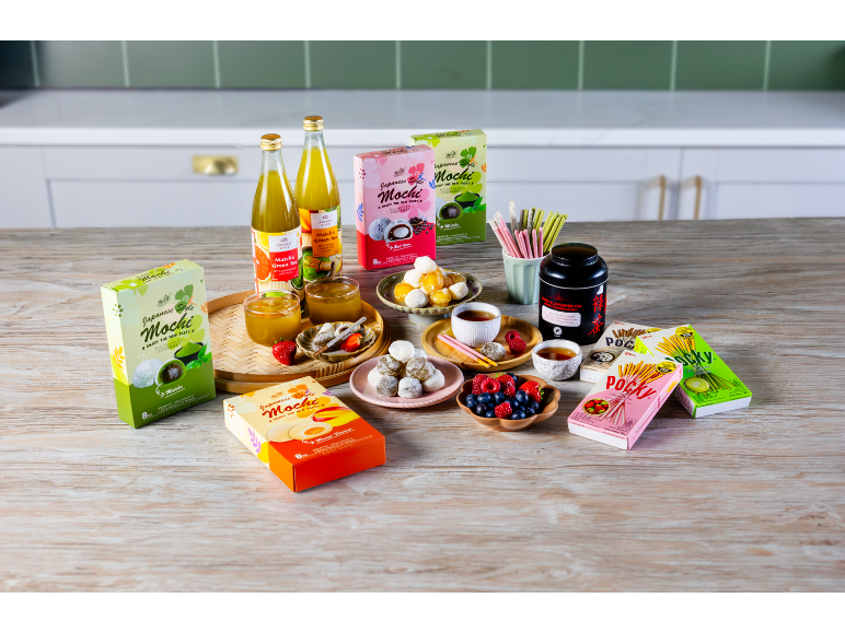 Assortiment de mochi de style japonais, de boissons au thé vert et de biscuits Pocky sur une table en bois.