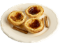 Trois tartelettes crémeuses Pastel de Nata avec de la cannelle sur une assiette blanche.