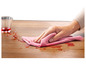 Une main essuie un liquide renversé sur une table en bois avec un chiffon rose.