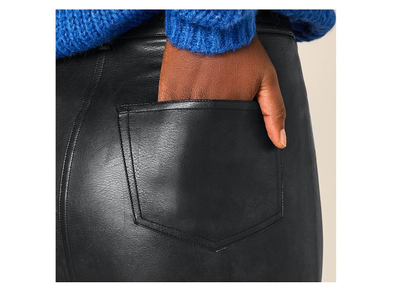 Femme à la peau foncée en pull bleu et jupe en similicuir noir, la main dans la poche.