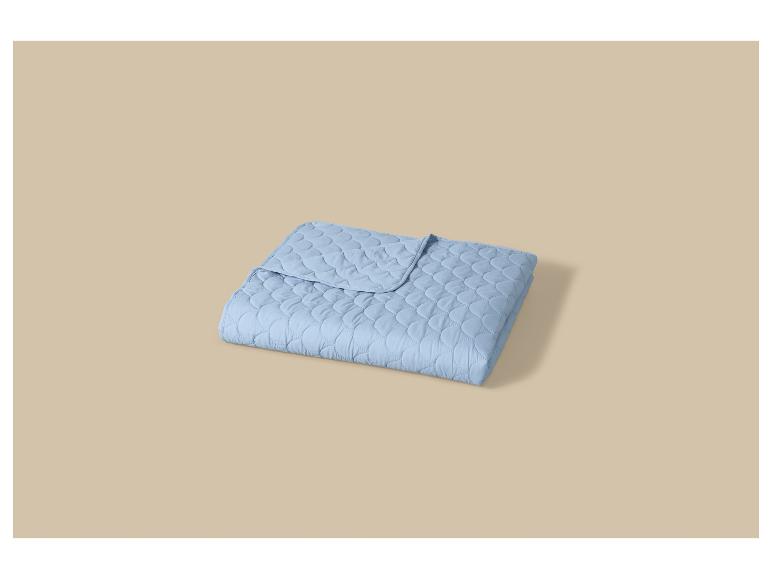 Couverture matelassée bleue pliée sur un fond beige.