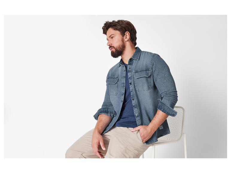 Un homme porte une chemise en jean et un pantalon beige.