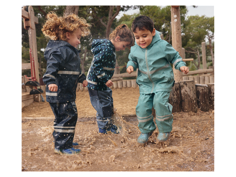 Trois enfants s'amusent dans une flaque d'eau avec leurs imperméables.
