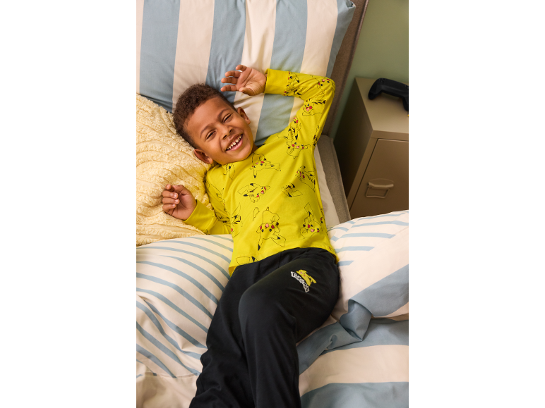Garçon en pyjama jaune à manches longues imprimé et pantalon noir allongé dans un lit.