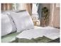 Oreillers et couette blancs avec drap vert et couverture dans une chambre.