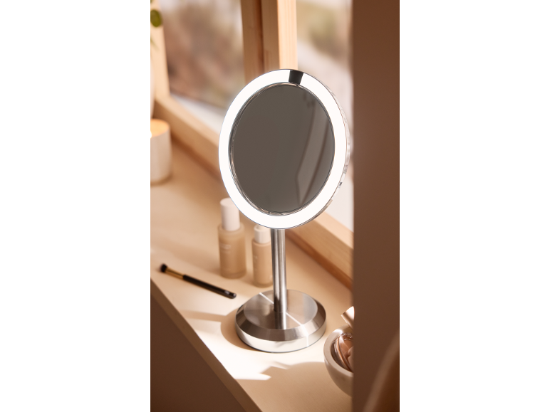 Miroir de maquillage rond avec éclairage LED sur un rebord de fenêtre ensoleillé.