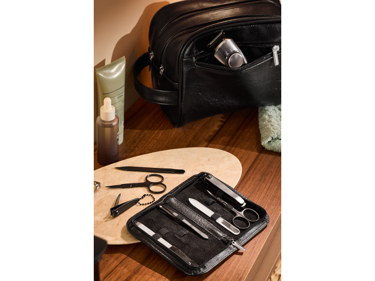 Trousse de toilette noire avec rasoir électrique, produits de soin et set de manucure sur une table en bois.