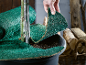 Main plaçant un tapis de protection vert pour plantes autour d'un arbre en pot, avec du bois de chauffage en arrière-plan.