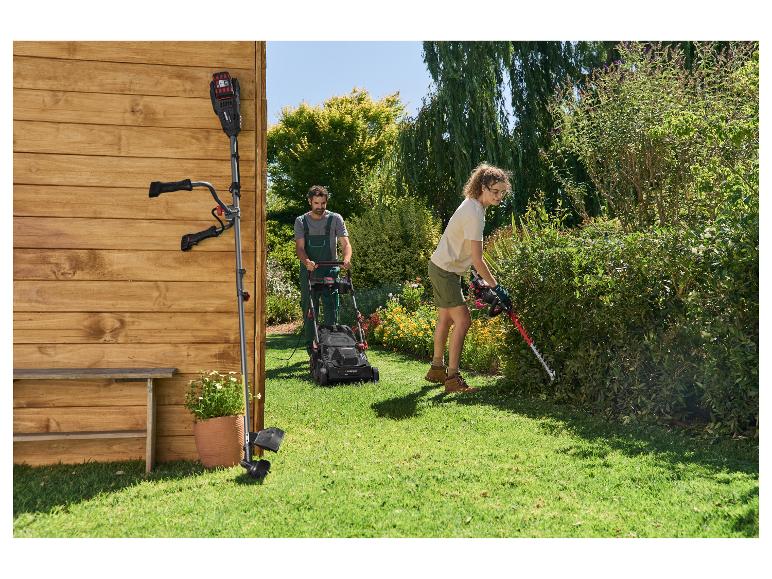 Homme tondant la pelouse avec une tondeuse et femme taillant la haie avec un taille-haie dans le jardin.
