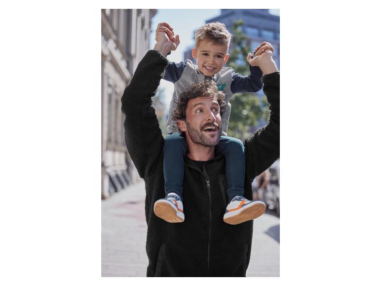Un homme porte son fils sur ses épaules, alors qu'il porte une veste en polaire noire.