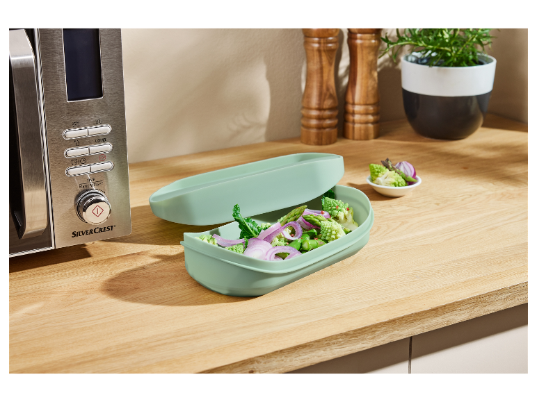 Four à micro-ondes SilverCrest et récipient vert clair contenant des légumes.