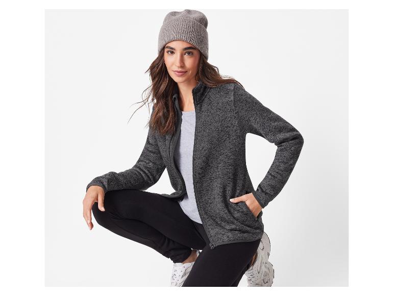 Femme en veste grise, pantalon noir et bonnet gris, accroupie.