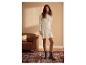 Femme en robe pull gris clair, collants marron et bottines grises, debout sur un tapis.
