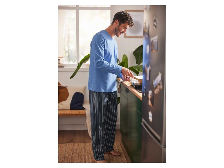 Un homme en pyjama bleu à rayures cuisine dans la cuisine.