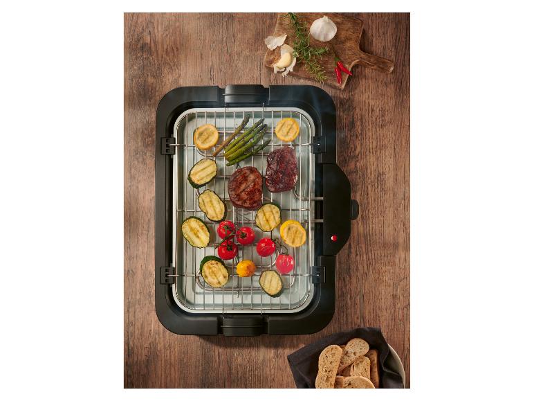Grill électrique avec viande et légumes grillés, épices et pain sur une table en bois.
