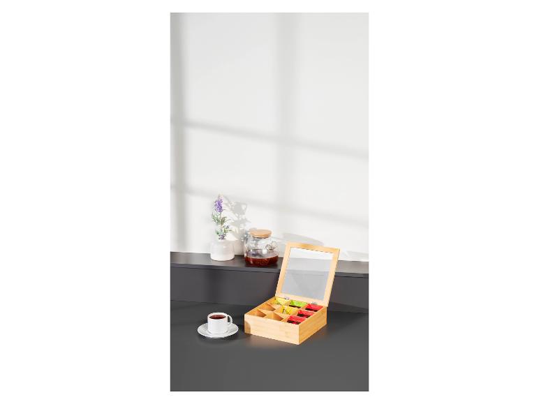 Boîte à thé en bambou avec compartiments et une tasse de thé sur une table sombre.