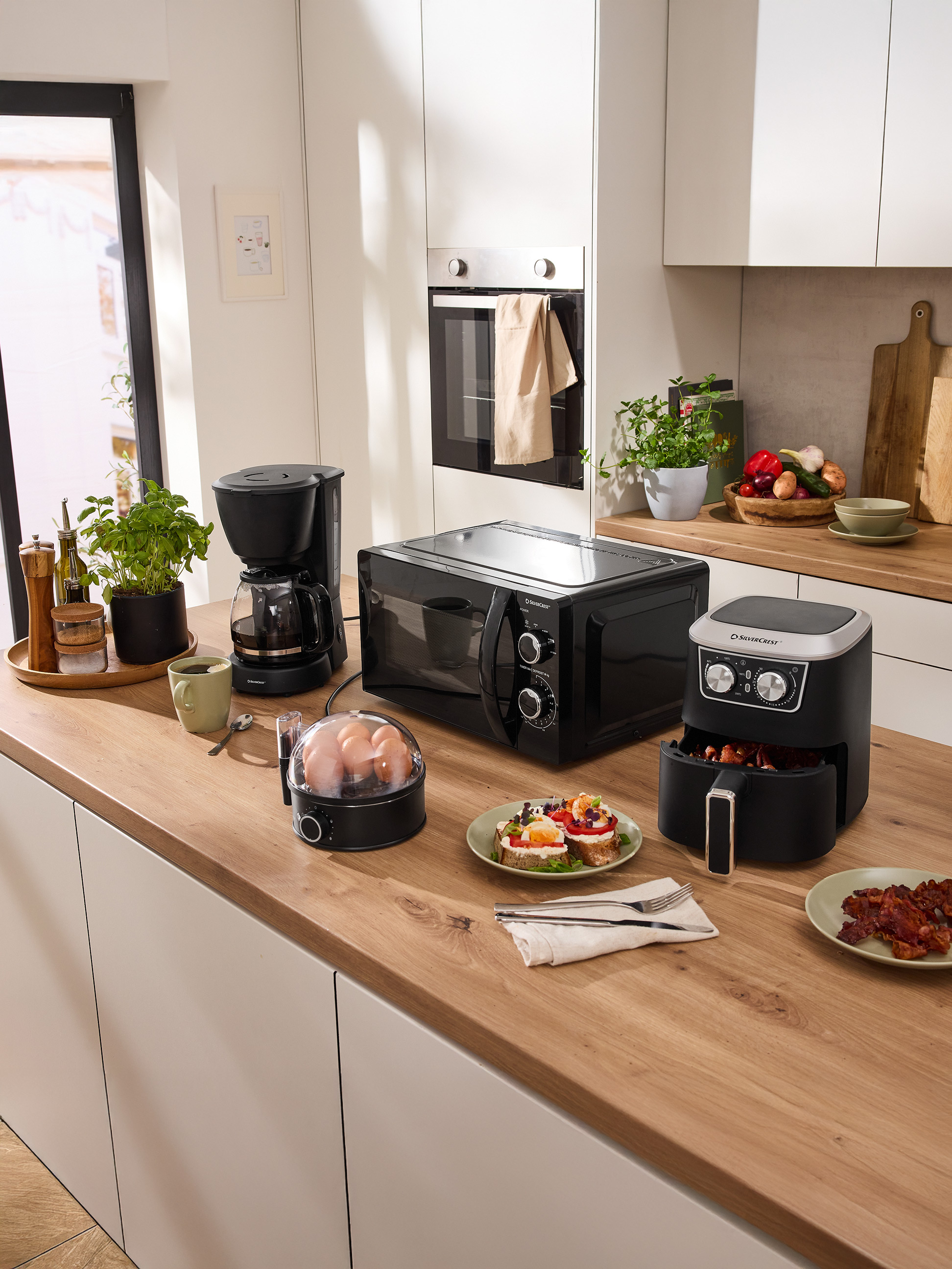 Plan de travail de cuisine avec micro-ondes SilverCrest, cafetière, friteuse à air et appareils de petit-déjeuner.