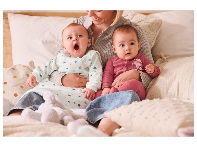 Une femme tient deux bébés en gigoteuses sur un lit.