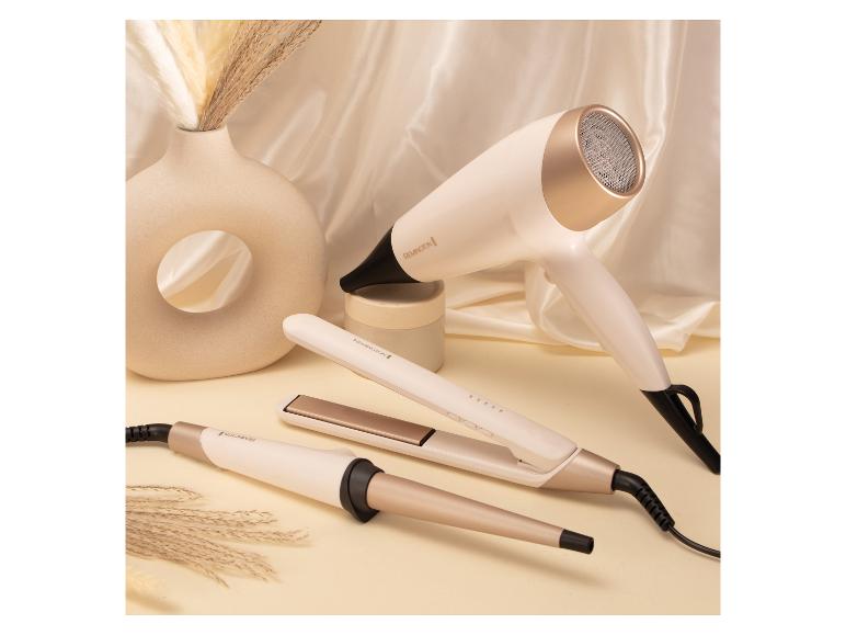 Sèche-cheveux, fer à lisser et fer à boucler sur fond crème avec un vase et des herbes de la pampa.