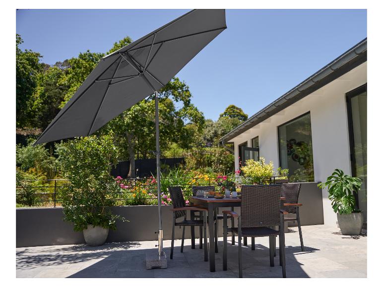 Ensemble de salle à manger d'extérieur avec parasol sur une terrasse, vue sur jardin et maison.
