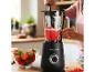 Femme préparant un smoothie aux fraises dans un mixeur noir, entourée de fraises fraîches.