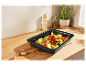 Plat à four noir contenant des légumes rôtis sur un comptoir en bois.