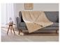Une couverture beige avec une texture de sherpa sur un canapé gris.