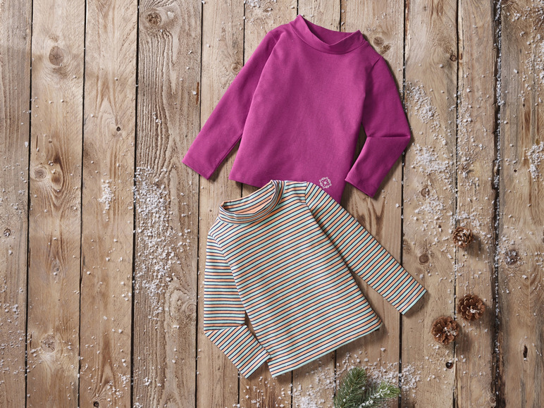 Deux t-shirts à manches longues sur un fond en bois avec de la neige : un t-shirt à manches longues rose et un t-shirt à manches longues rayé.