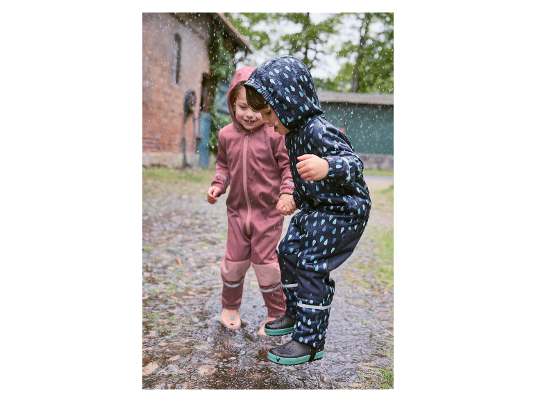 Deux enfants en combinaisons de pluie Reima éclaboussent dans une flaque.