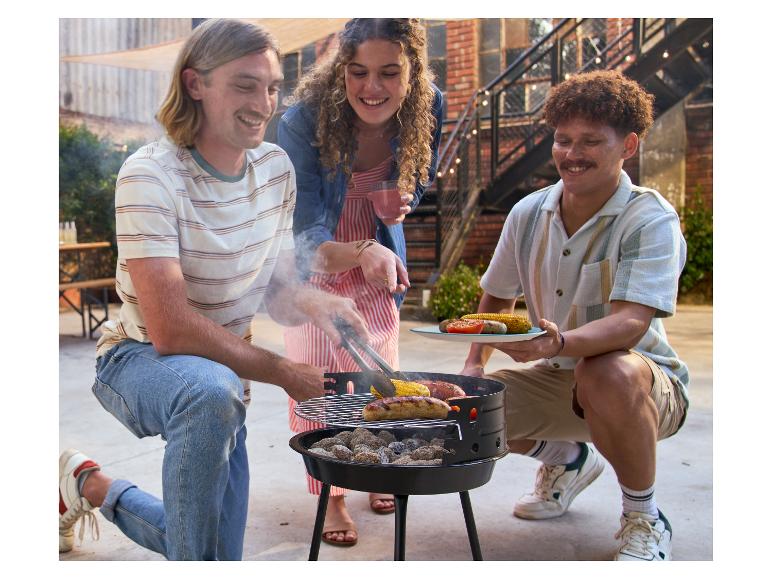 Amis préparant des saucisses et du maïs au barbecue en plein air.