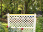 Un treillis en bois blanc avec un motif en losanges dans un jardin vert.