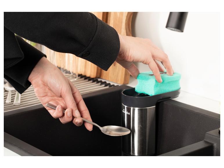 Mains lavant une cuillère dans un évier de cuisine avec une éponge et un distributeur de savon.