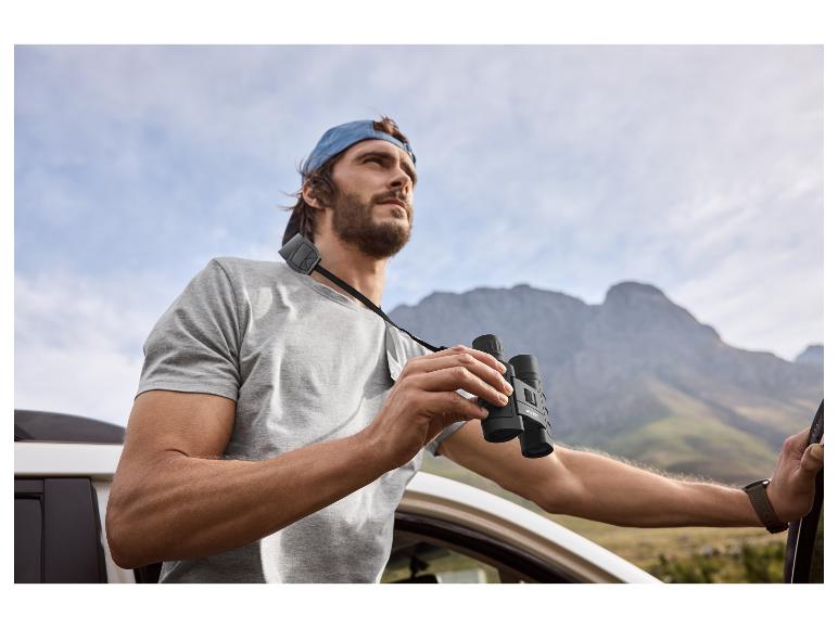 Homme avec des jumelles et une casquette regardant les montagnes depuis une voiture.