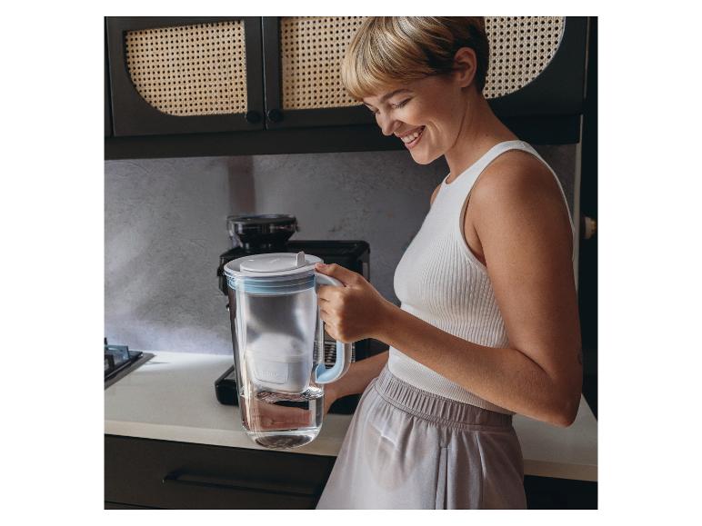 Une femme tenant une carafe filtrante en verre BRITA dans une cuisine.