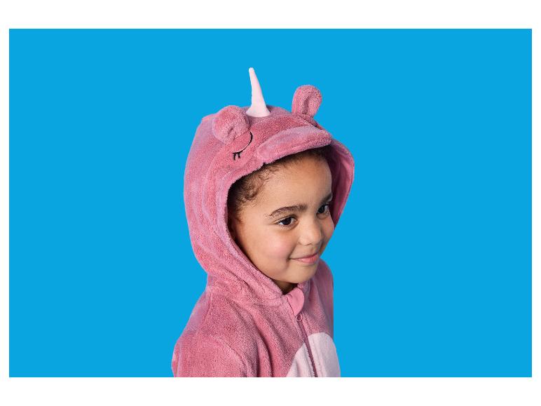 Fille en pyjama licorne rose, souriant sur fond bleu.