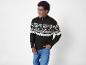 Un homme avec un pull noir à motif géométrique et un jean bleu.