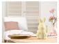 Une figurine de lapin blanche sur une table en bois avec un plateau en bois et des fleurs roses.